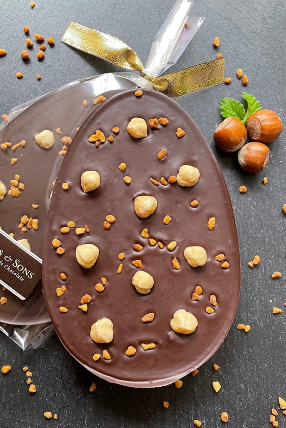 Go Nuts dark chocolate easter egg bar topped with whole hazelnuts and chopped, roasted caramelised hazelnut pieces. In clear packaging tied with a gold ribbon bow