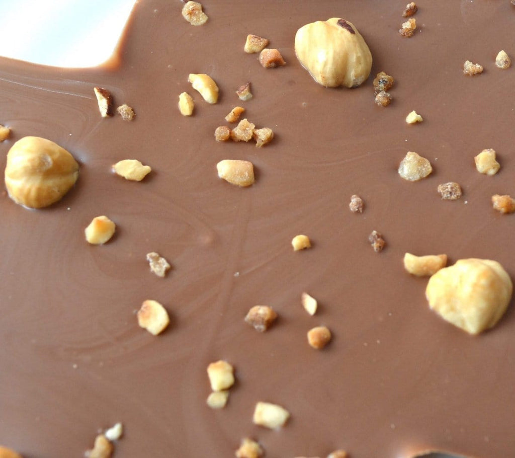 close up of milk chocolate topped with whole and chopped hazelnuts